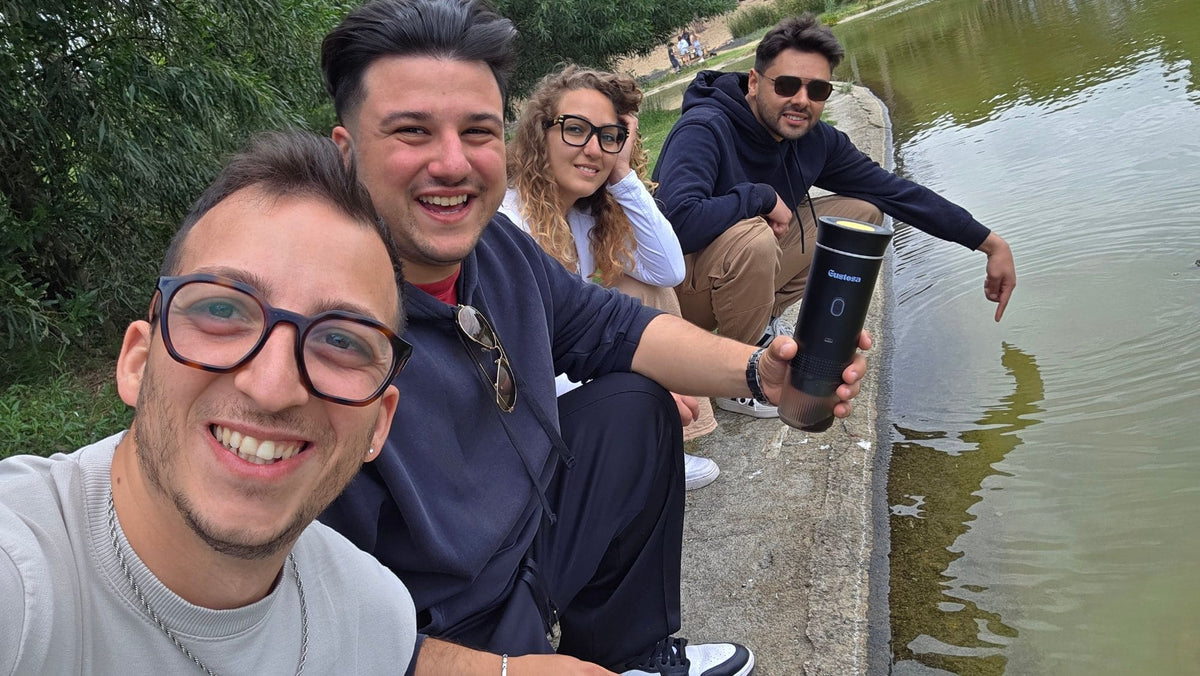Four smiling team members sitting together by a lakeside, one holding a MyGustosa portable espresso maker, capturing the moment the Gustosa brand was born after the founders quit their jobs and committed everything to building a real portable coffee experience.