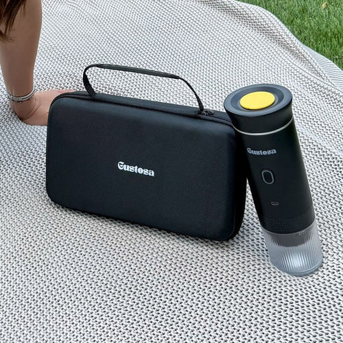 The Gustosa hard-shell carrying case and MyGustosa portable espresso maker placed side by side on a white knit blanket outdoors, showcasing the complete and compact travel coffee setup.