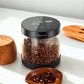 The Gustosa Electric Vacuum Container filled with whole coffee beans on a white surface surrounded by wooden accessories, with the smart LED lid showing vacuum status, battery level and timer settings.