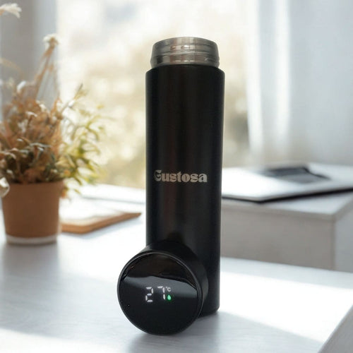 The Gustosa Smart Bottle in matte black standing on a desk next to a plant and a laptop, with the LED temperature display on the base showing 27°C, highlighting the real-time temperature monitoring feature of the smart insulated bottle.