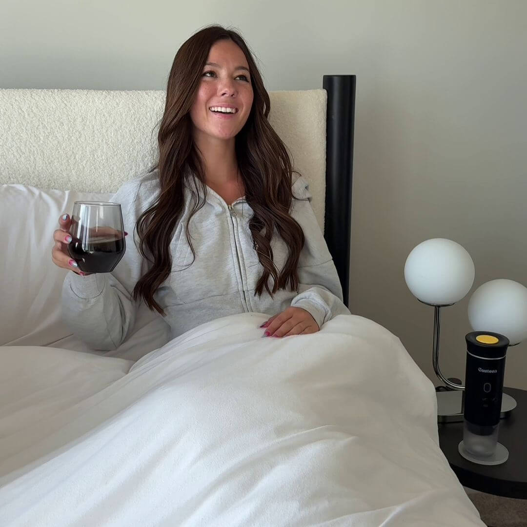 Smiling woman enjoying coffee in bed with Gustosa portable coffee maker on bedside table – comfort and convenience at home